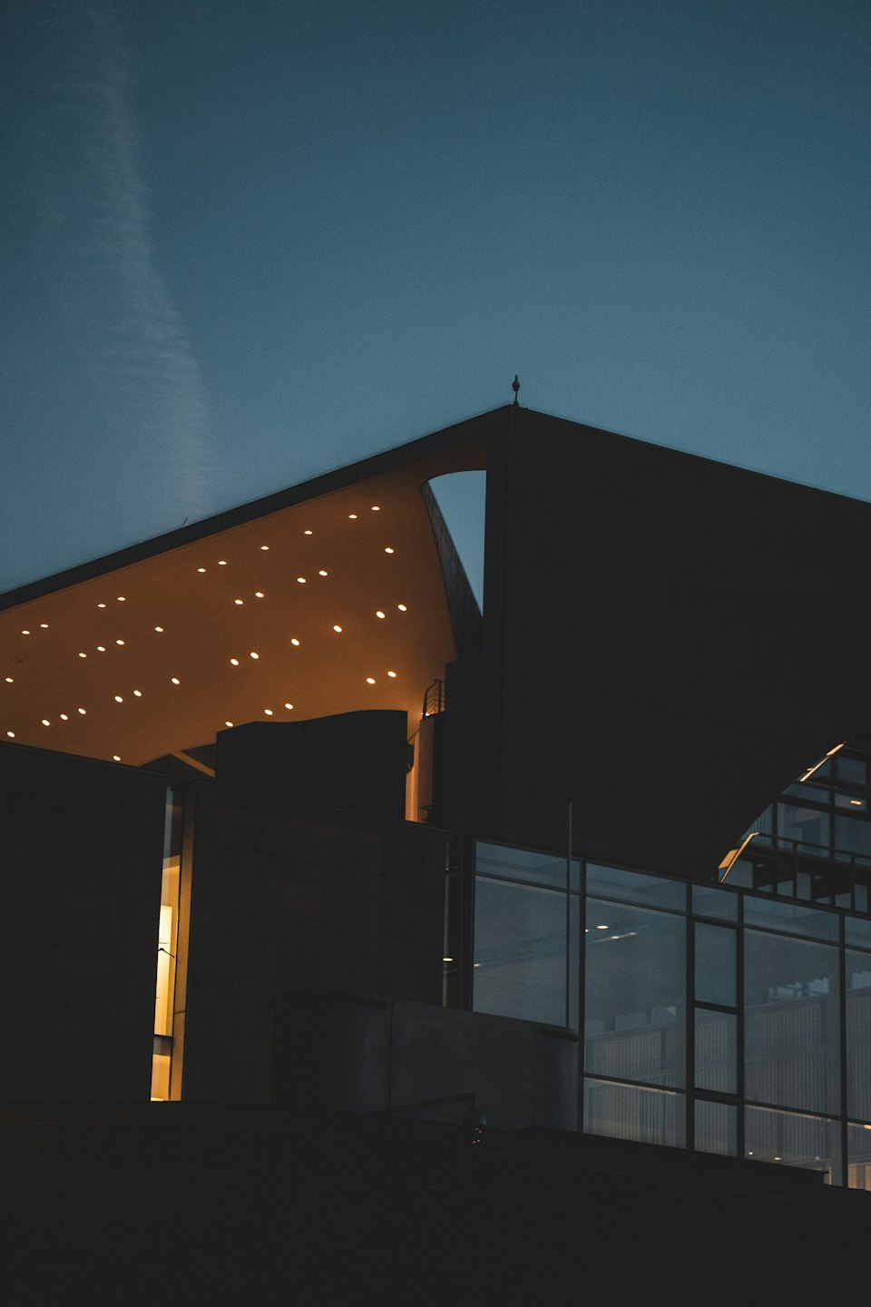 Modernes Gebäude mit eckigem Dach, beleuchtet in der Dämmerung.